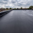 Wide expanse of a large flat roof covered in dark charcoal 1.2mm EPDM rubber membrane with a black metal edge trim along the parapet, damp under an overcast British sky