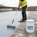 Roofer applying grey GRP roof restoration coating across a full roof surface, RUBBER ROOF UK branded tin