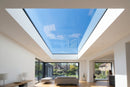 Interior view looking up through a frameless flat roof skylight showing daylight and clean glass ceiling reveal