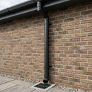 Textured black round aluminium downpipe installed down a brick wall with clips and shoe