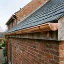 Bright polished copper half round guttering fitted along the eaves of a heritage-style brick building, correctly supported on brackets with closed ends
