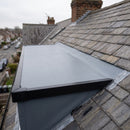 Close-up of the dormer roof edge: black kerb trim and corner on the side, EPDM membrane running up under the bottom row of slates at the back