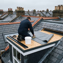 Roofer bedding the one-piece EPDM membrane onto a dormer roof deck with a roller, water-based adhesive and kerb trims ready at the edge - cold applied, no torch
