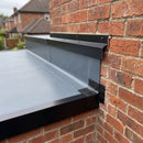 Close-up of the EPDM upstand against a brick house wall covered by the black wall flashing trim, with the side kerb trim and a corner patch sealing the junction