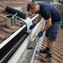 Roofer rolling EPDM rubber lining into a long gutter run on a tiled roof – whole-house Finlock gutter refurbishment