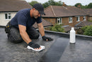 Roofer cleaning a weathered EPDM rubber flat roof with membrane cleaner, restoring the dark grey finish