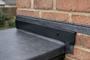 Black metal wall flashing trim fixed to a brick wall where an EPDM rubber flat roof meets the house