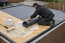 Roofer bonding grey EPDM rubber membrane to a freestanding garage timber roof deck with water-based adhesive - cold applied, no heat
