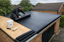 Roofer unrolling a single one-piece EPDM rubber membrane across a brick garage flat roof