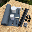 Garden room rubber roof kit contents laid out on an OSB deck: 1.2mm EPDM membrane, deck adhesive, contact adhesive, kerb and gutter trims, four corners, rollers, scissors and fixings