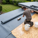 Installer sweeping a one-piece 1.2mm EPDM sheet into wet water-based adhesive on a garden room OSB roof deck
