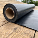 Close-up of a partially unrolled black root barrier membrane roll on a timber roof deck, showing the woven-reinforced surface texture and cut edge