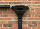 Black cast iron fluted rainwater hopper mounted on a brick wall feeding a downpipe