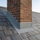 Grey lead-free flashing dressed around a brick chimney stack on a UK pitched slate roof