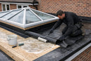 Installer bonding EPDM rubber membrane to a timber orangery roof deck with water-based adhesive and roller around the glass lantern upstand - cold applied, no heat required