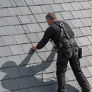 Roofer wearing a black fall arrest harness and rope while working on a pitched slate roof