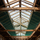 Green safety net rigged beneath open roof timber rafters during re-roofing work