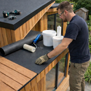 Roofer applying EPDM adhesive on garden room flat roof with black metal edge trims and roller - garden office roofing UK