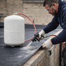 Roofer applying EPDM spray adhesive to flat rubber roof edge - professional flat roofing adhesive UK