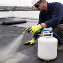 Roofer spraying EPDM contact adhesive onto flat roof surface with rubber roofing membrane roll - UK roofing supplies