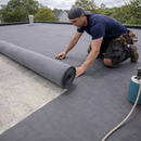 Roofer unrolling 1.2mm EPDM rubber roofing membrane on flat roof for garden room - EPDM membrane UK