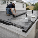 Roofer unrolling EPDM rubber membrane on a garage outbuilding flat roof with adhesive