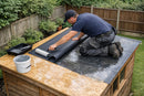 Installer rolling EPDM rubber membrane onto a timber shed roof deck with cold-applied water-based adhesive, no flames or heat required