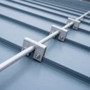 Close-up of an aluminium snow guard clamp gripping the raised seam of a standing seam metal roof panel with the connecting tube passing through the clamp