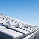 Row of aluminium snow guard clamps and connecting tube fitted along the eave of a standing seam metal roof with light snow cover